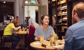 Die Cafébar im Berner Generationenhaus: an kleinen, runden Tischen sitzen Menschen und essen, im Hintergrund die Bücherwand.